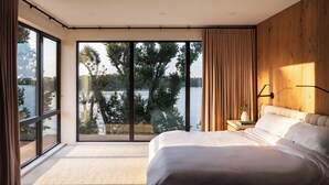 Un dormitorio con un ventanal que ofrece vistas a un lago y árboles.