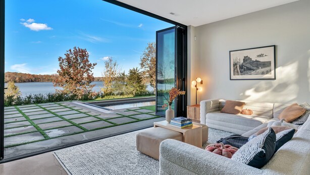 Un salón moderno con un gran ventanal que da a un patio con vistas a un lago y árboles.