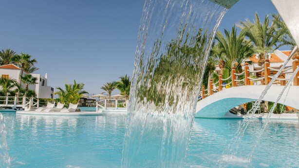 A pool with a water feature, palm trees, and a bridge. - Aparthotel Parque Santiago III (Arona)