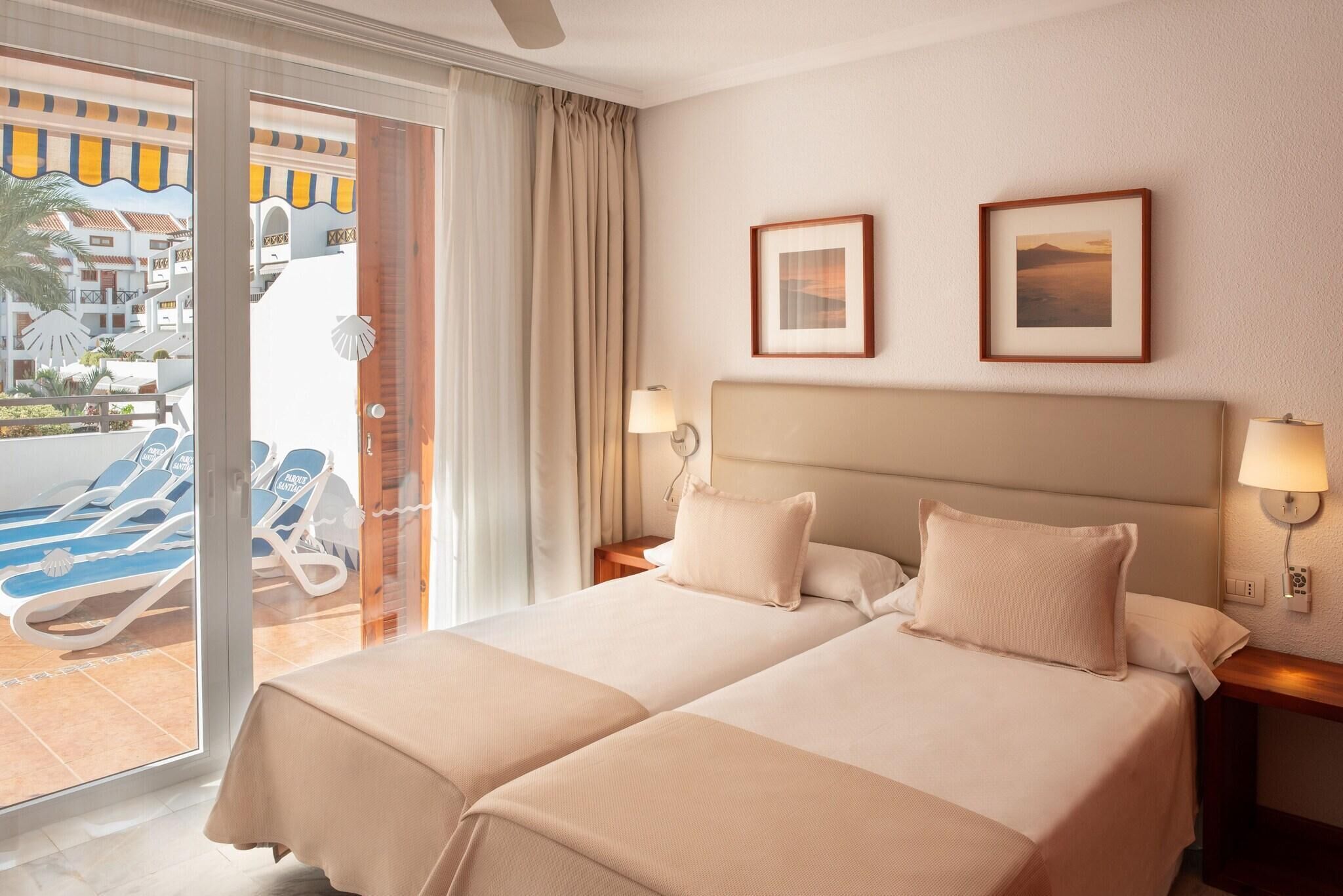 Habitación de hotel con dos camas, un balcón con sillones de descanso y dos cuadros en la pared.