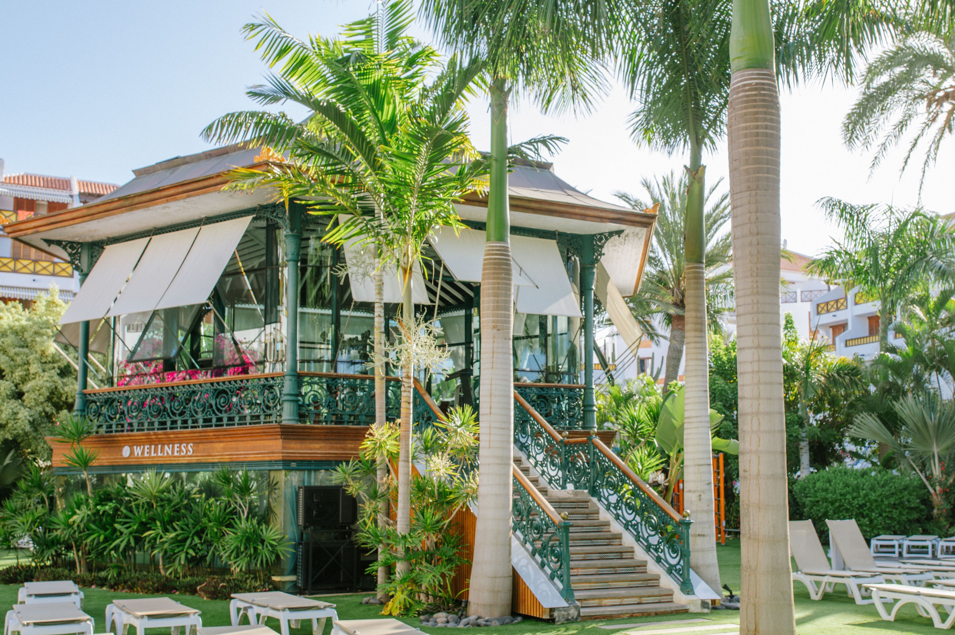 A wellness center with a covered outdoor seating area, a staircase, and palm trees.