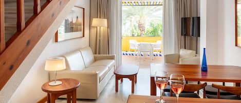 A hotel room with a wooden staircase, a sofa, a dining table with wine glasses, and a view of the outdoors.