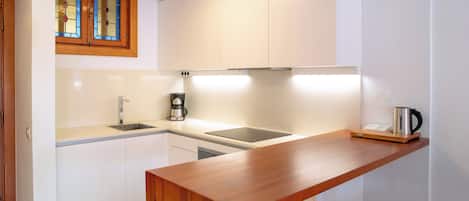 A modern kitchen with white cabinets, a wooden countertop, and a coffee maker.