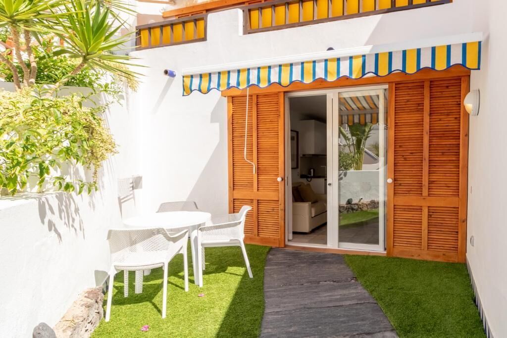 A small patio with a white table and chairs, a wooden door, and a small garden area.