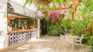 An outdoor patio with wooden flooring, white wicker chairs, and a bar area with a glass enclosure. - Aparthotel Parque Santiago III (Arona)