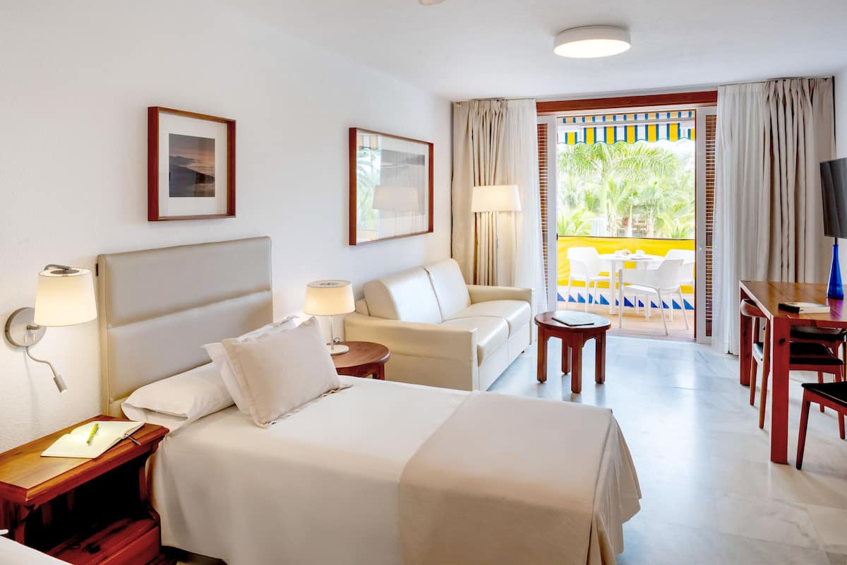 Quarto de hotel com cama, sofá, escrivaninha e televisão.