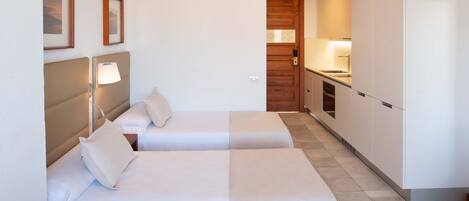 A compact hotel room with two beds, a kitchenette, and a ceiling fan.
