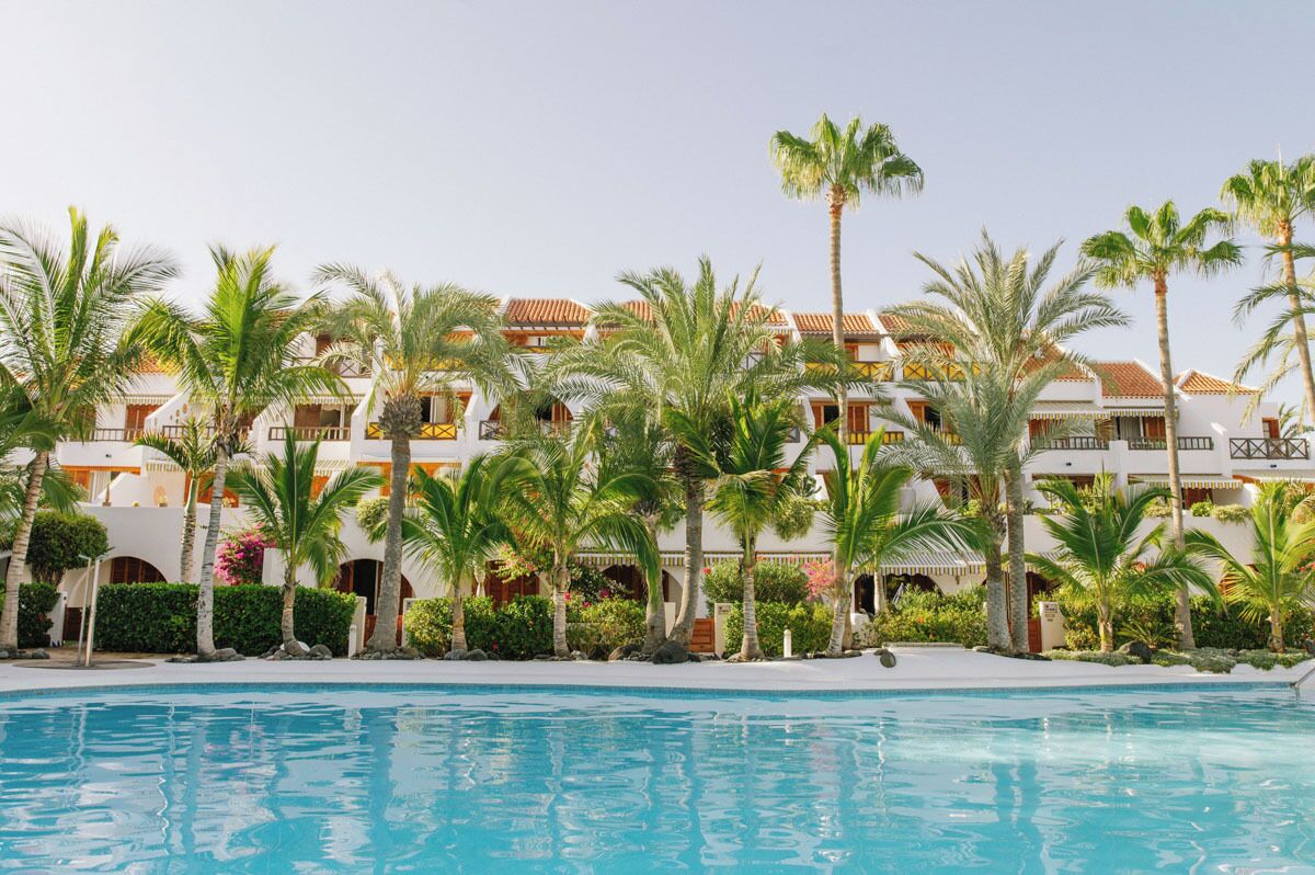 A resort with multiple-story buildings, a swimming pool, and palm trees.
