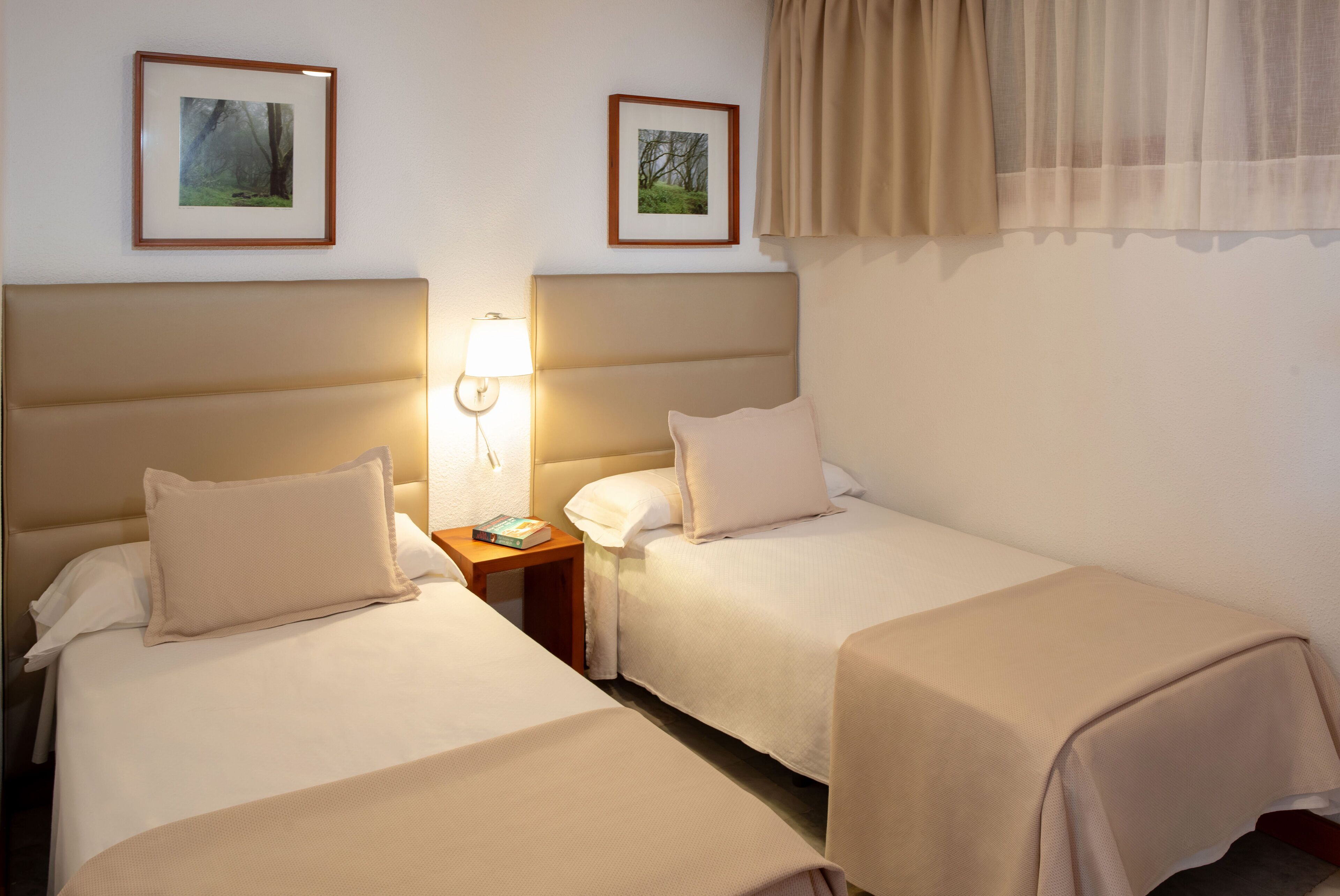 Habitación de hotel con dos camas, una lámpara de noche y cuadros en la pared.