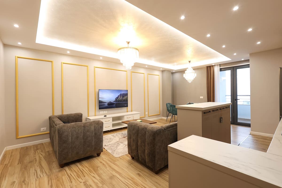 A modern living room with a flat-screen TV, two sofas, a coffee table, and a kitchen area with a counter and cabinets.