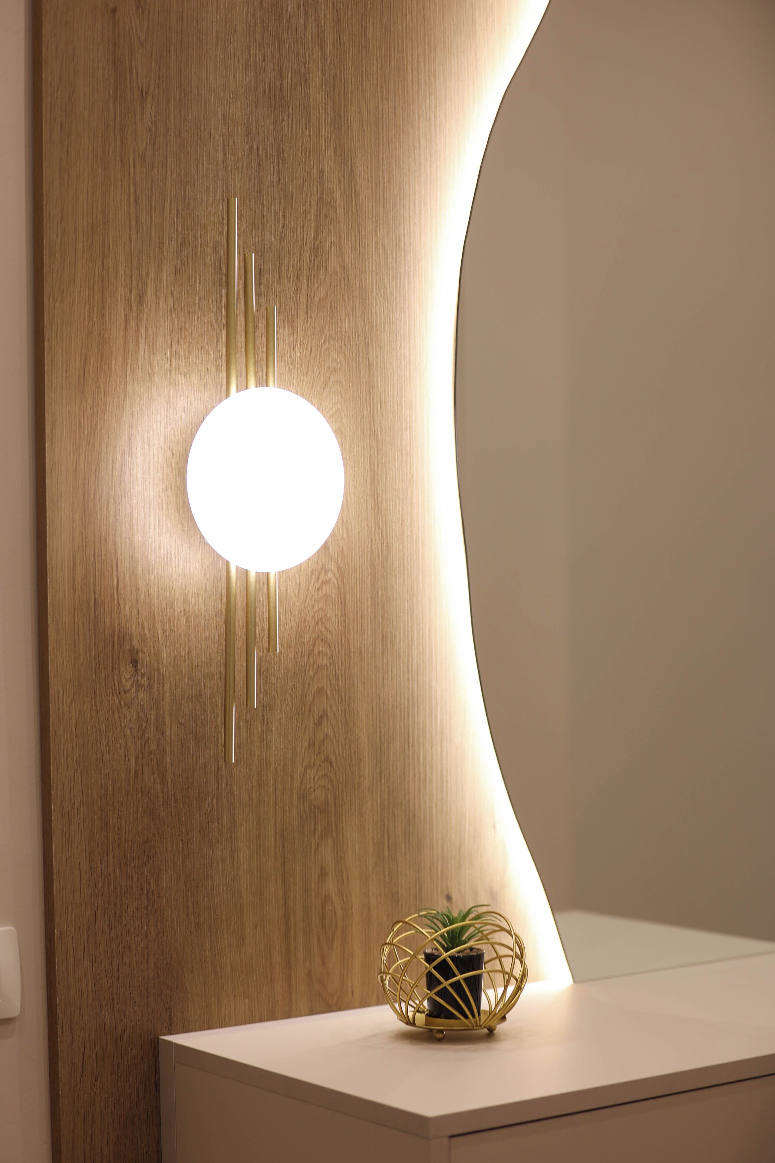 Une salle de bain moderne avec un mur en bois, un luminaire rond et une petite plante posée sur le comptoir.