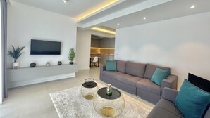 Een moderne woonkamer met een grijze bank, een salontafel en een aan de muur bevestigde televisie.