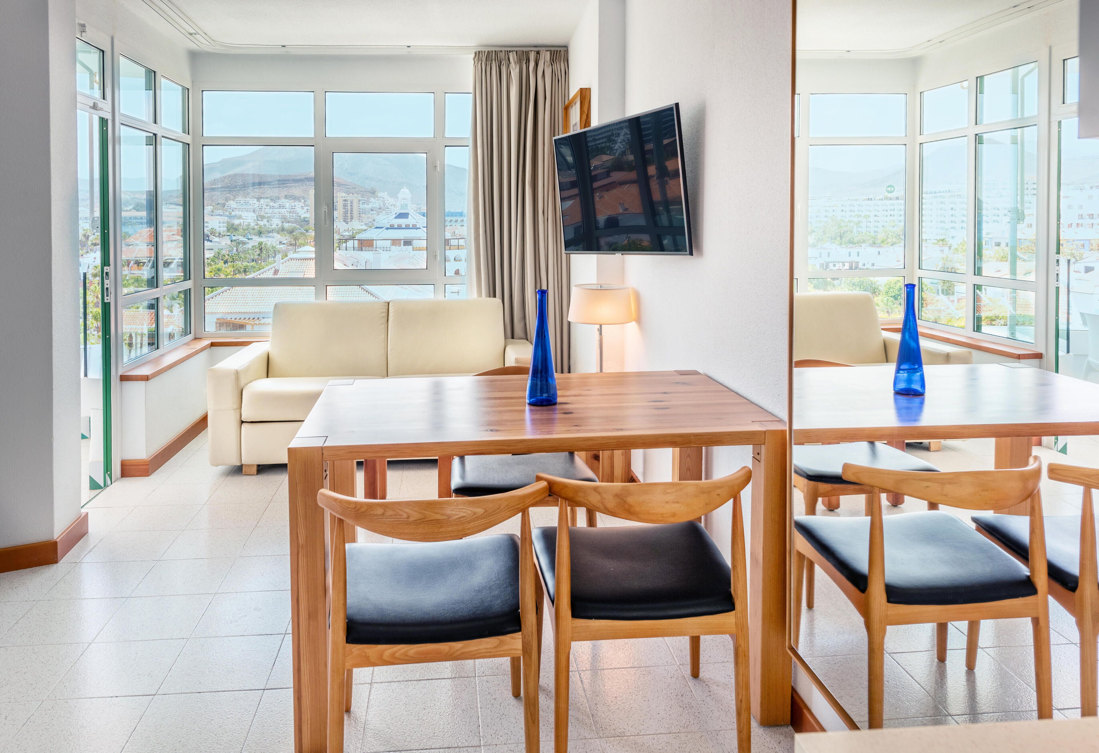 Ein modernes Hotelzimmer mit Essbereich, großen Fenstern mit Stadtblick, einem Flachbildfernseher und einer Couch.
