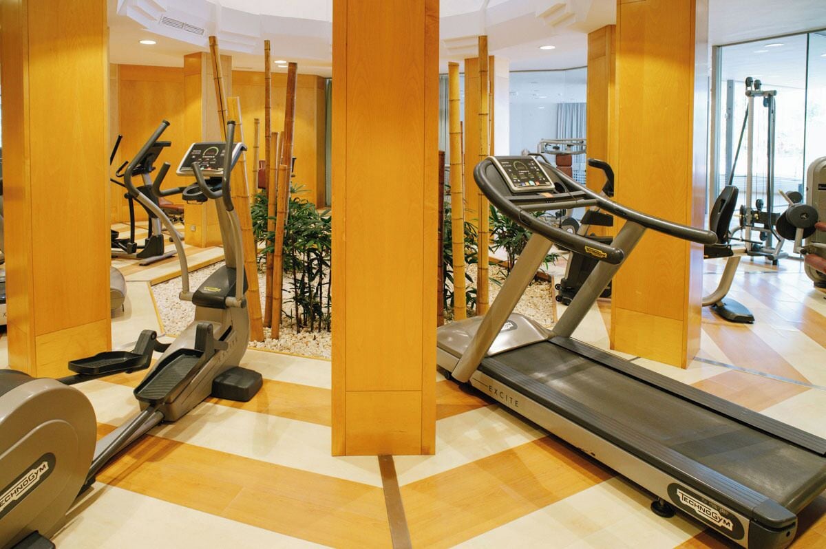Une salle de sport équipée de machines de cardio, avec des piliers en bois et un sol à carreaux.