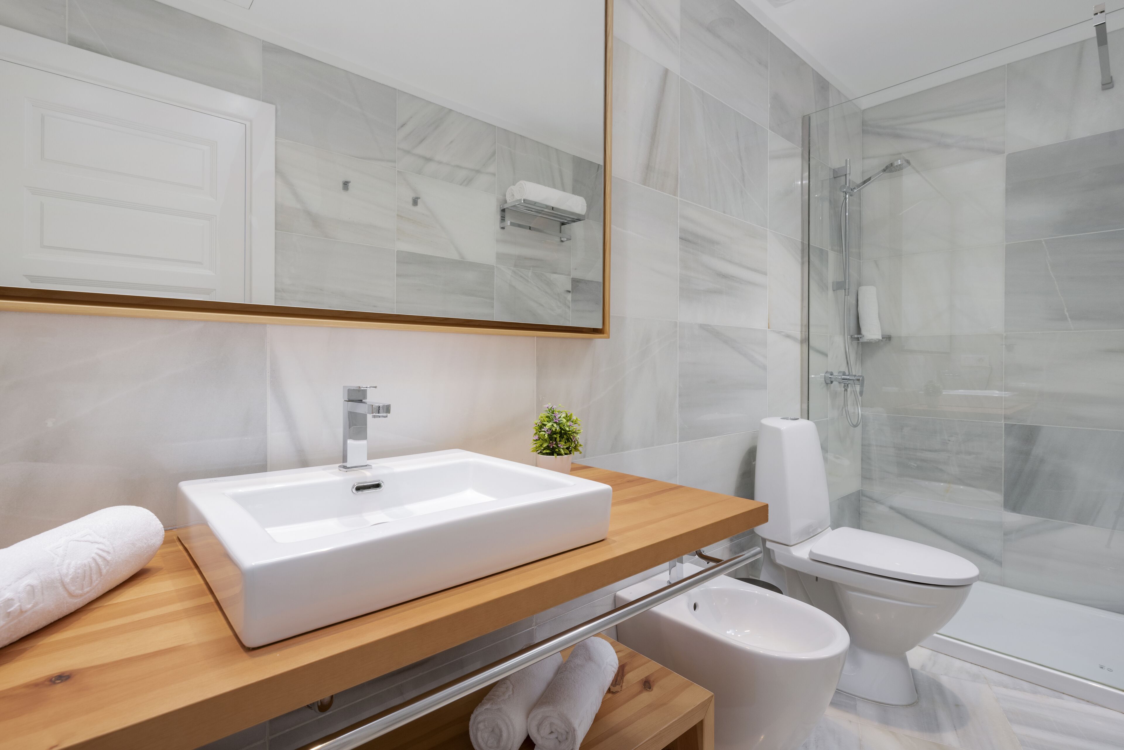 A modern bathroom with a large mirror, a white sink, a toilet, and a shower area.
