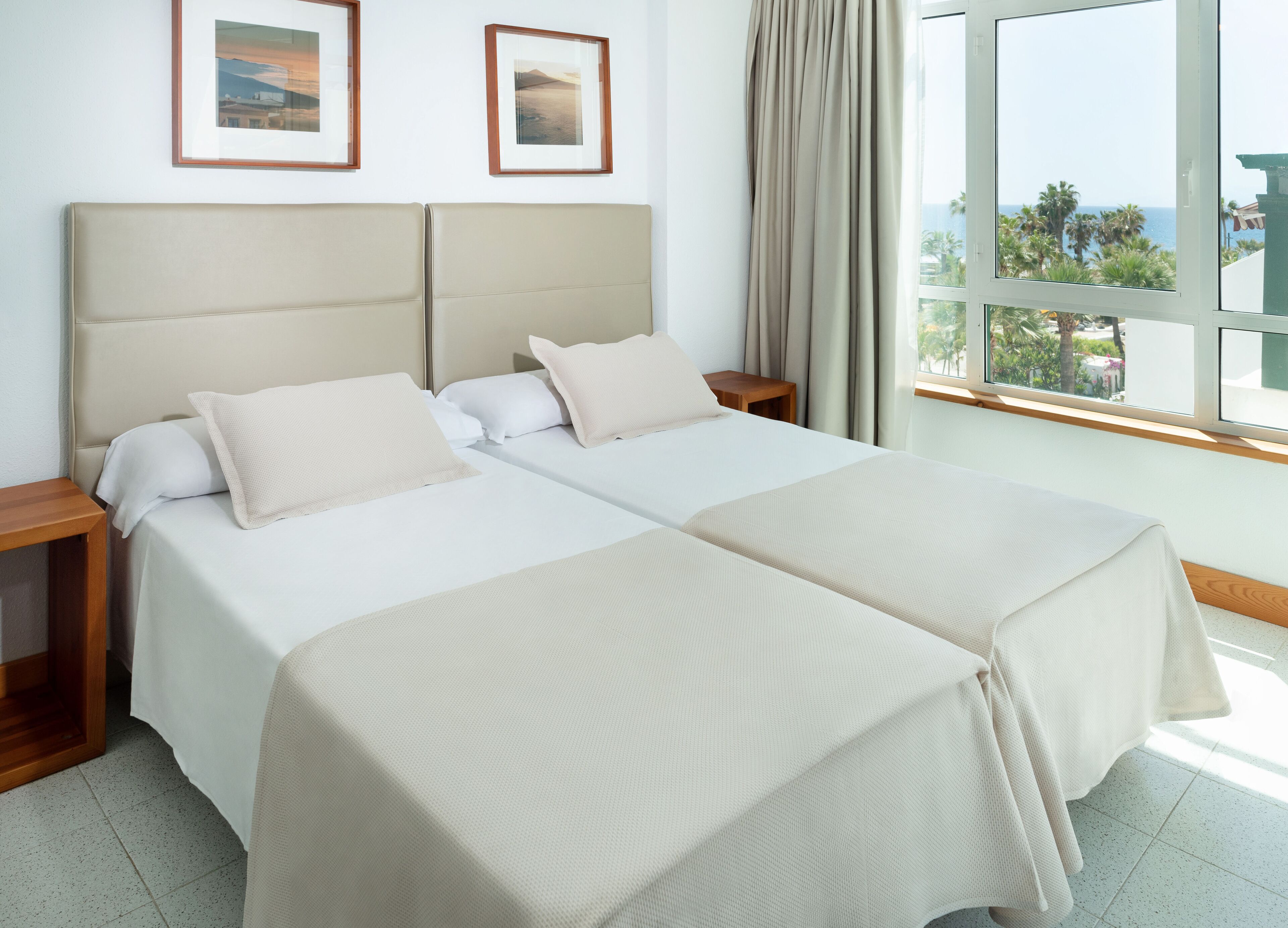 A double bed room with two nightstands, a large window with a view, and two framed pictures on the wall.