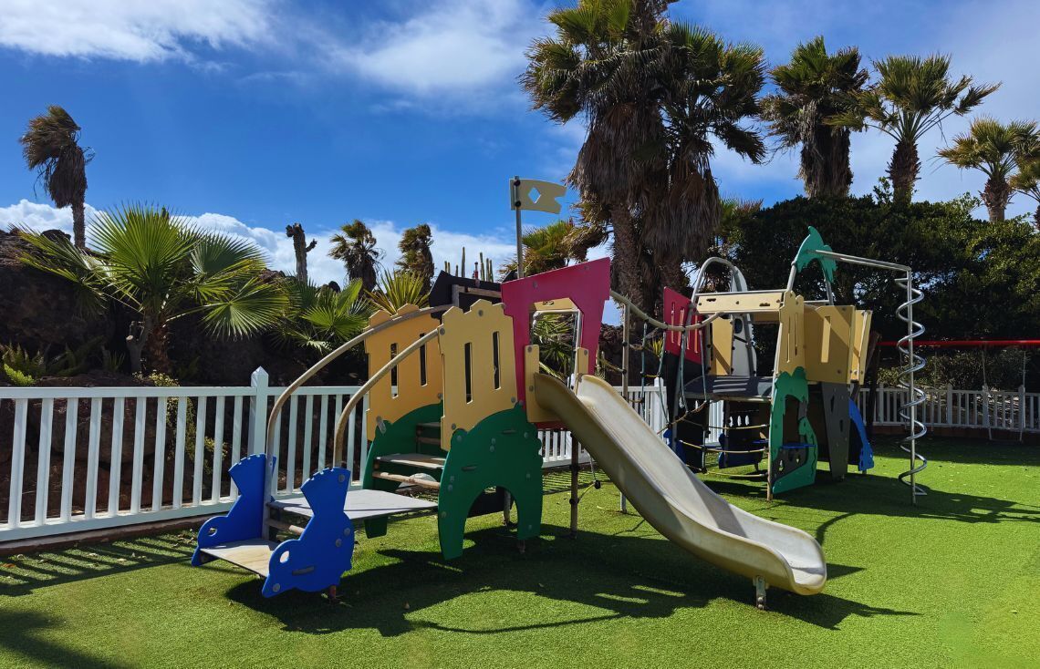 Un parque infantil con tobogán, estructuras para escalar y una zona delimitada.
