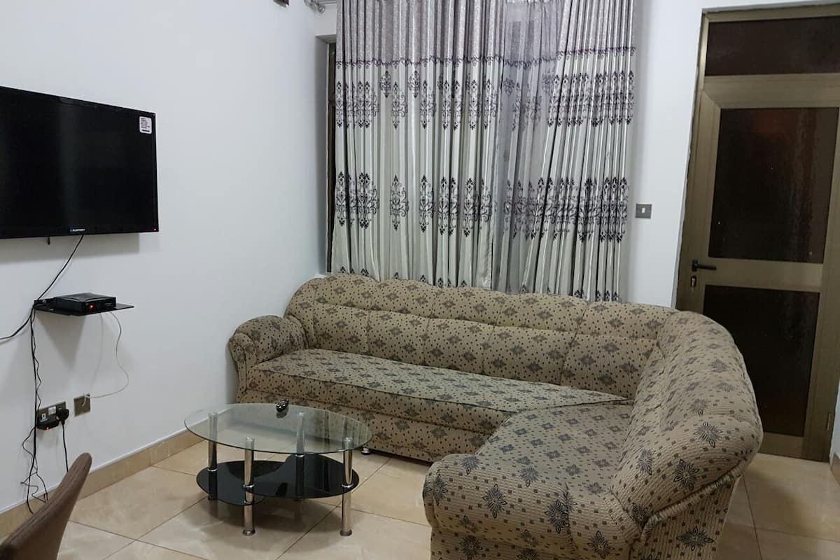A living room with a sofa, a glass coffee table, a flat-screen TV mounted on the wall, and a door with a glass panel.