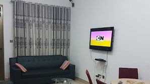 A living room with a sofa, coffee table, TV, and dining area. - 2Bedrooms Private. Apart. Junction Mall (Accra)