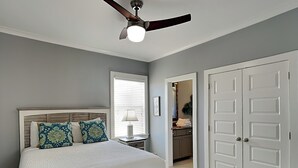Ein Schlafzimmer mit einem Bett, einem Deckenventilator, einem Fenster und einer Tür.