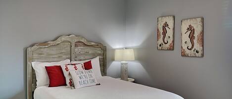 Un dormitorio con una cama, una mesita de noche, una lámpara y dos adornos de caballitos de mar en la pared.