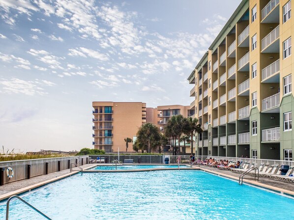 Una piscina con sillones de descanso y un edificio con varios balcones al fondo.