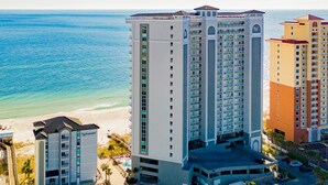 Een hoog hotel met meerdere balkons, een zwembadgedeelte en uitzicht op strand en zee.