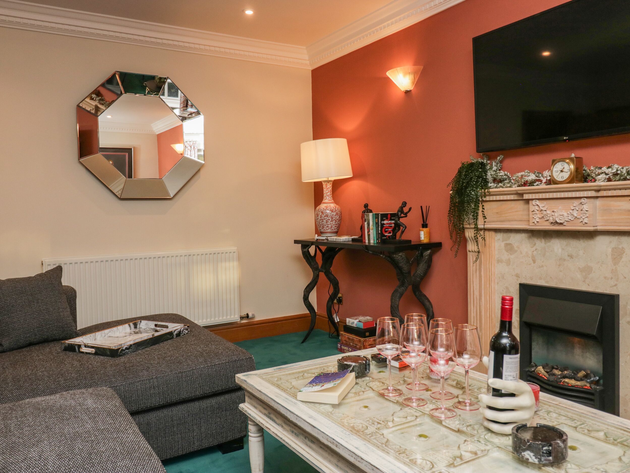 A living room with a fireplace, a television, a mirror, and a table with wine glasses.