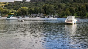 A calm lake with several boats docked near a small building surrounded by trees. - Lakeside View (Ulverston)