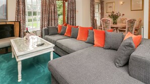 A living room with a grey sectional sofa, orange cushions, a white coffee table, and a dining area with floral chairs. - Lakeside View (Ulverston)
