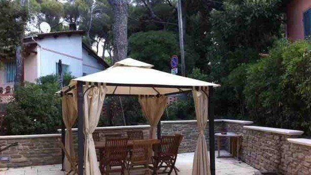 An outdoor patio with a wooden table and chairs under a canopy. - Villetta a Castiglioncello (Rosignano Solvay-Castiglioncello)