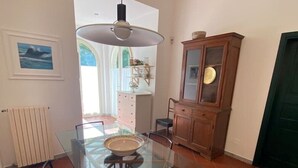 A dining area with a glass table, two chairs, a hanging light fixture, a cabinet, and a radiator. - Villetta a Castiglioncello (Rosignano Solvay-Castiglioncello)