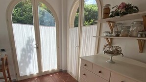 A room with a tiled floor, a white dresser with drawers, a shelf with jars, and a chair. - Villetta a Castiglioncello (Rosignano Solvay-Castiglioncello)