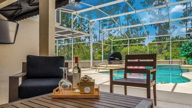 A covered outdoor seating area with a pool view, a grill, and a bottle of wine on a table. - Pool & Spa Oasis/Golf Retreat/Near Disney/3BR Home (davenport)