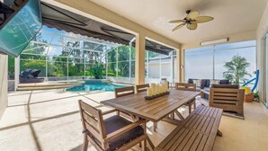 An outdoor patio with a pool, wooden furniture, and a ceiling fan. - Pool & Spa Oasis/Golf Retreat/Near Disney/3BR Home (davenport)
