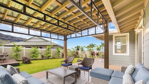 Um alpendre coberto com móveis de exterior, vista para o quintal e uma casa ao fundo.