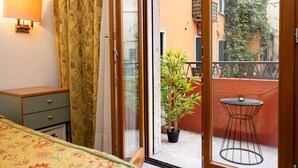 A bedroom with a bed, a nightstand, a lamp, a sliding glass door leading to a balcony with a potted plant and a small table. - CAMELIA ROOMS VENICE GUESTHOUSE (Mestre)