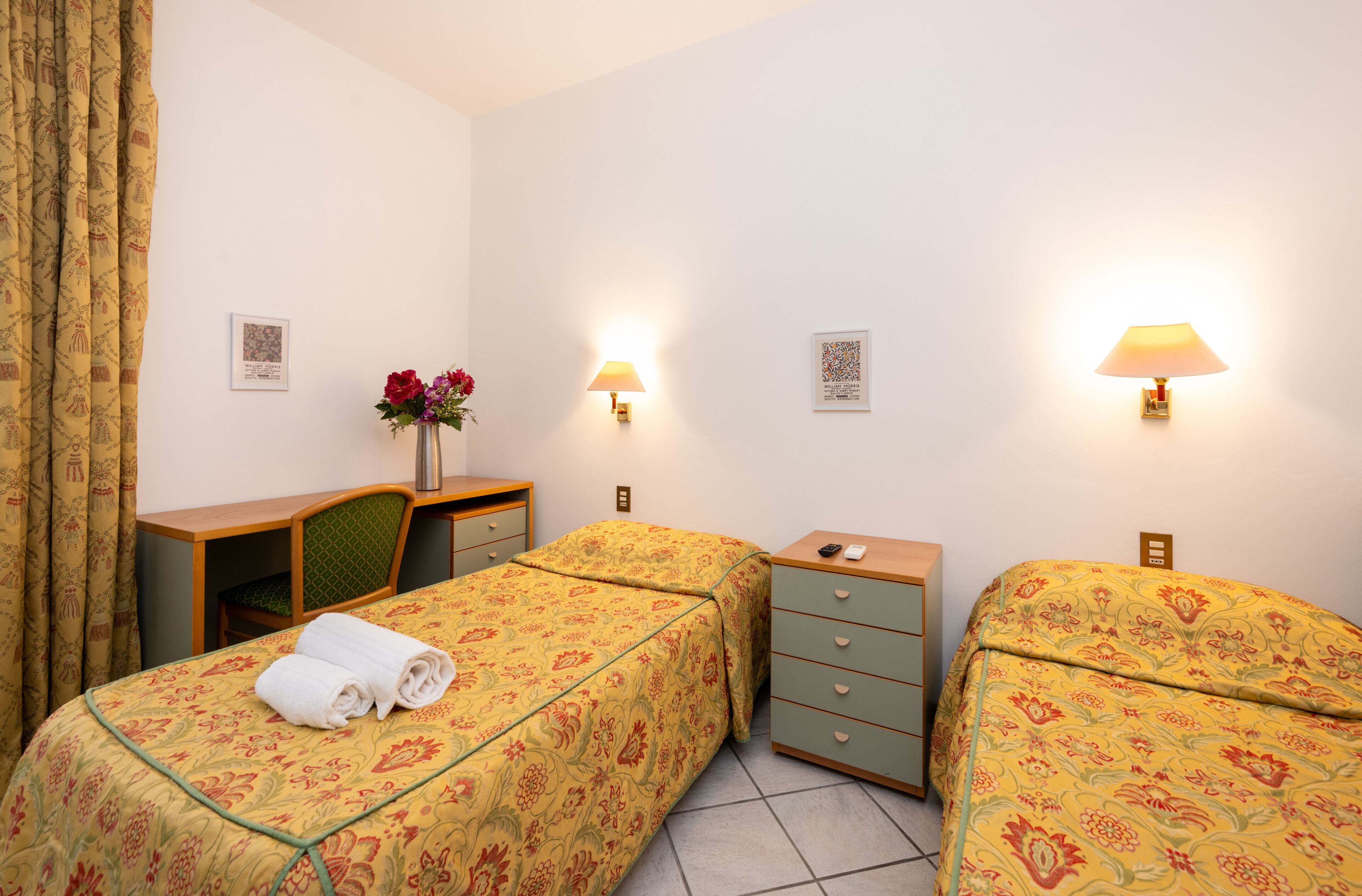 Habitación de hotel con dos camas, un escritorio, una silla, un aparador y dos lámparas de pared.