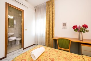 A hotel room with a bed, a desk, a chair, a bathroom with a sink and bidet, and a window with curtains. - CAMELIA ROOMS VENICE GUESTHOUSE (Mestre)