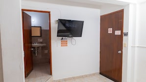 Une pièce avec un téléviseur fixé au mur, une porte en bois et un sol carrelé.