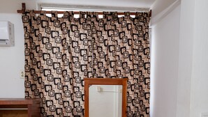 Une pièce avec un bureau en bois, un miroir, un petit tabouret et un rideau à motifs.