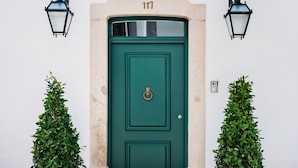 Une porte verte portant le numéro 117, flanquée de deux plantes en pot et de deux lanternes fixées au mur.
