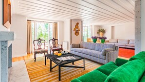 Un salon comprenant un canapé, un divan vert, un fauteuil à motifs, une table basse et une cheminée.