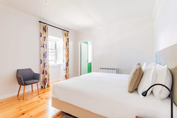 A bedroom with a bed, a chair, and a window with curtains. - Villa Azzurra Cascais 5BR (Cascais)