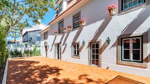 Un bâtiment blanc avec de nombreuses fenêtres, dont certaines sont dotées de volets, et des jardinières fixées au mur extérieur.