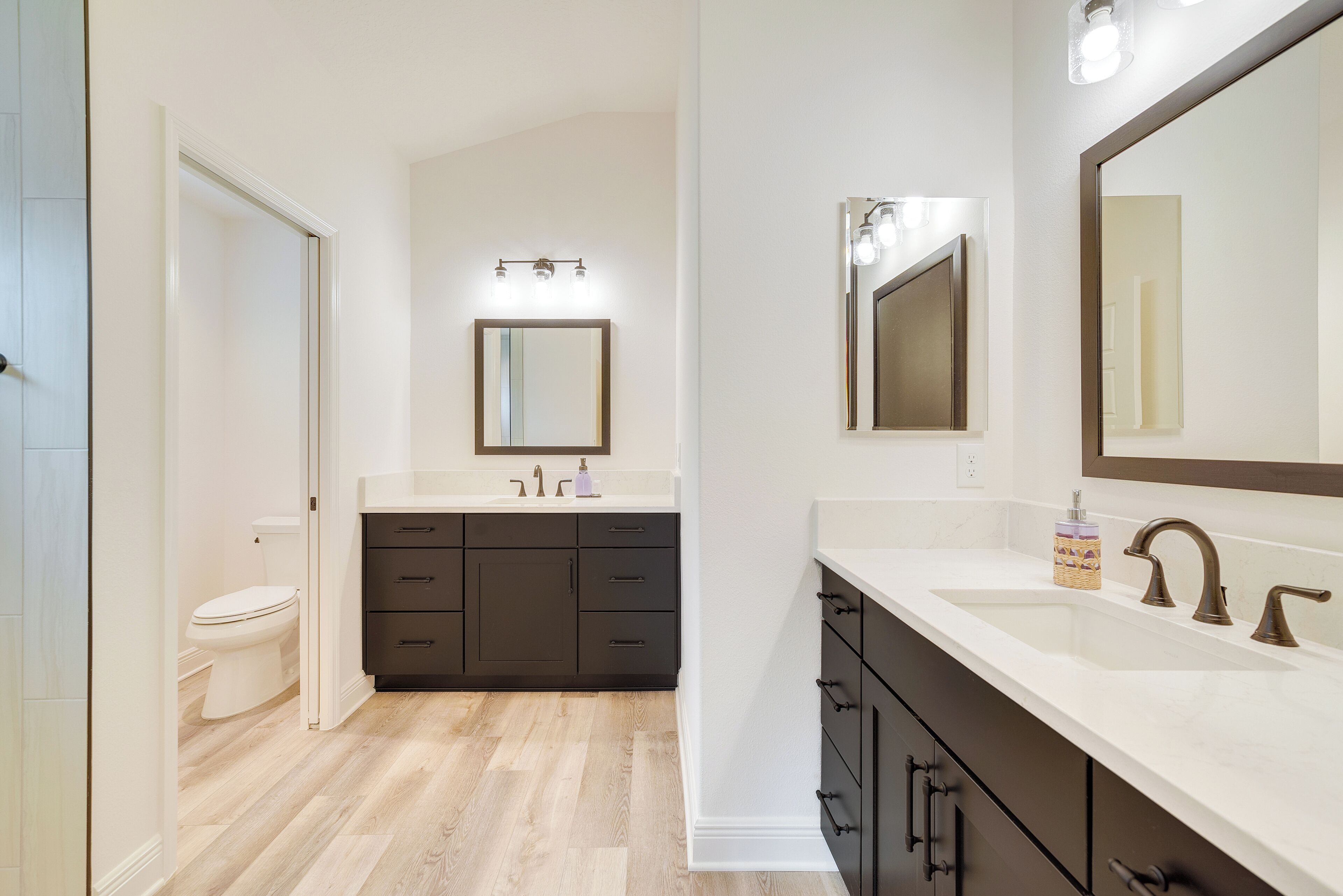 A modern bathroom with a white sink, dark cabinets, and a large mirror.