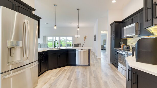 A modern kitchen with black cabinets, stainless steel appliances, and a wooden floor. - Pool Access & Screened Patio: Home in The Villages (Okahumpka)