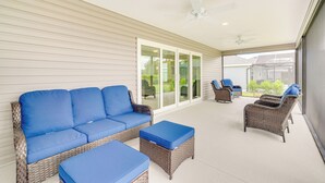 A covered patio with wicker furniture, including a sofa and ottomans, and a ceiling fan. - Pool Access & Screened Patio: Home in The Villages (Okahumpka)