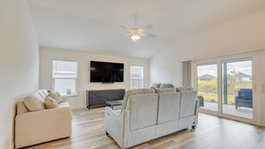 A spacious living room with a large grey sofa, a flat-screen TV mounted on the wall, and a ceiling fan. - Pool Access & Screened Patio: Home in The Villages (Okahumpka)