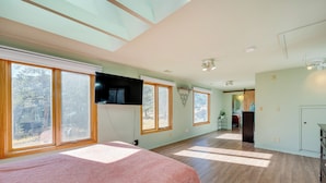 A spacious room with large windows, a flat-screen TV mounted on the wall, and a wooden floor. - 17 Mi to Town: Peaceful Pet-friendly Golden Cabin! (Golden)